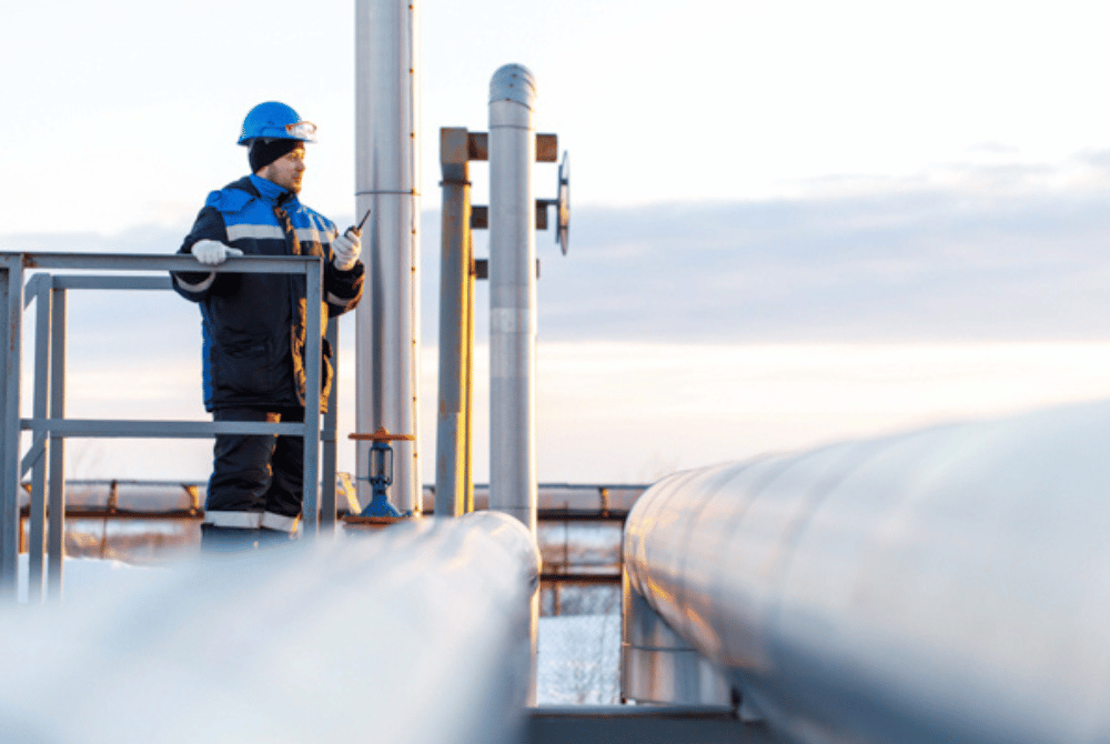 Worker in safety gear standing on an industrial platform beside large pipeline infrastructure