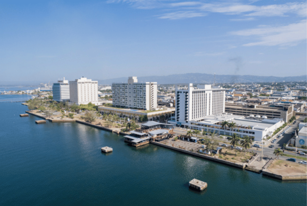 Aerial photograph of a Jamaican coastal city with commercial buildings along the waterfront.