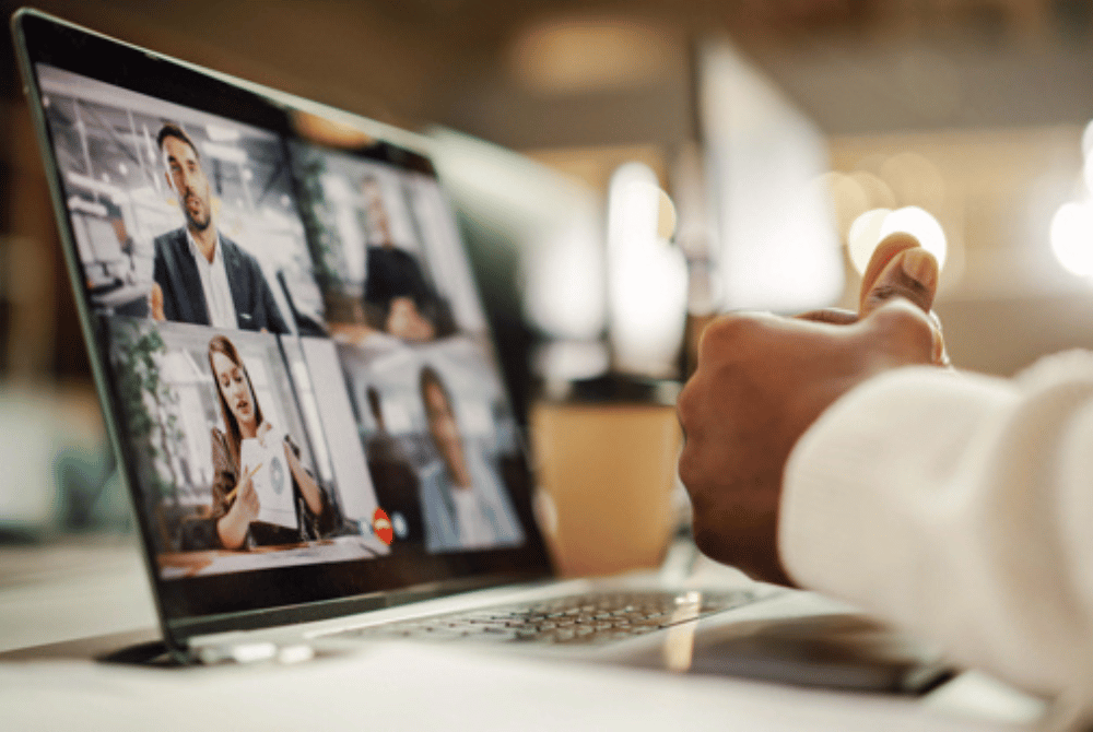 Person viewing a video conference call with multiple participants on a laptop screen.