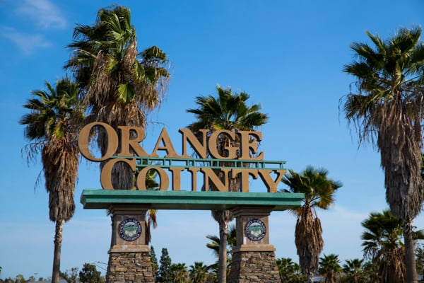 Orange County entrance sign framed by palm trees against a clear blue sky