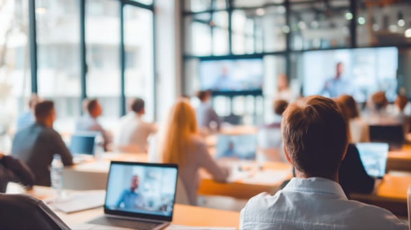 People listening to a presentation in a conference room with screens and laptops visible