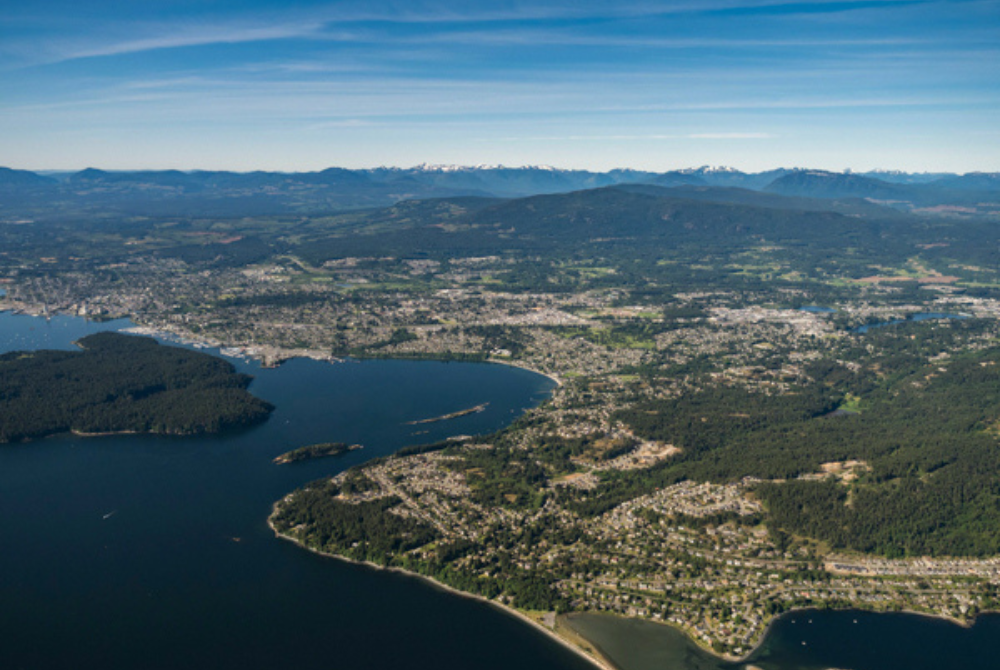 Aerial view of Nanaimo with coastline, residential communities, forested hills, and mountain ranges