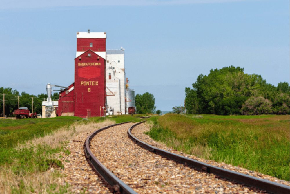 Railway tracks leading toward a grain elevator in Ponteix, Saskatchewan, surrounded by open grassland