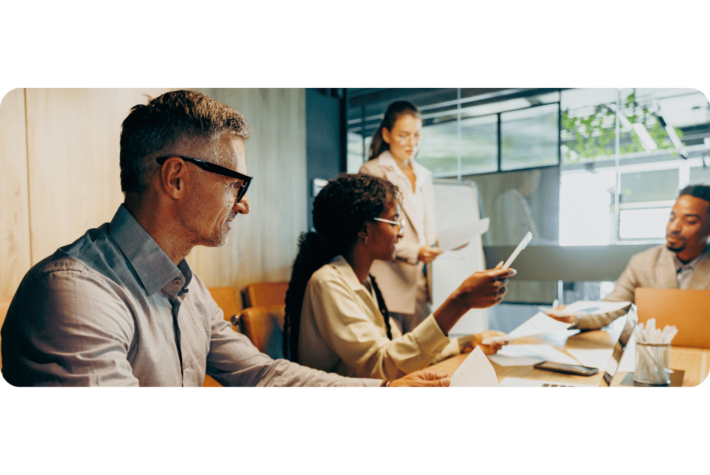 Four people collaborating in a meeting room, reviewing documents and discussing materials around a conference table