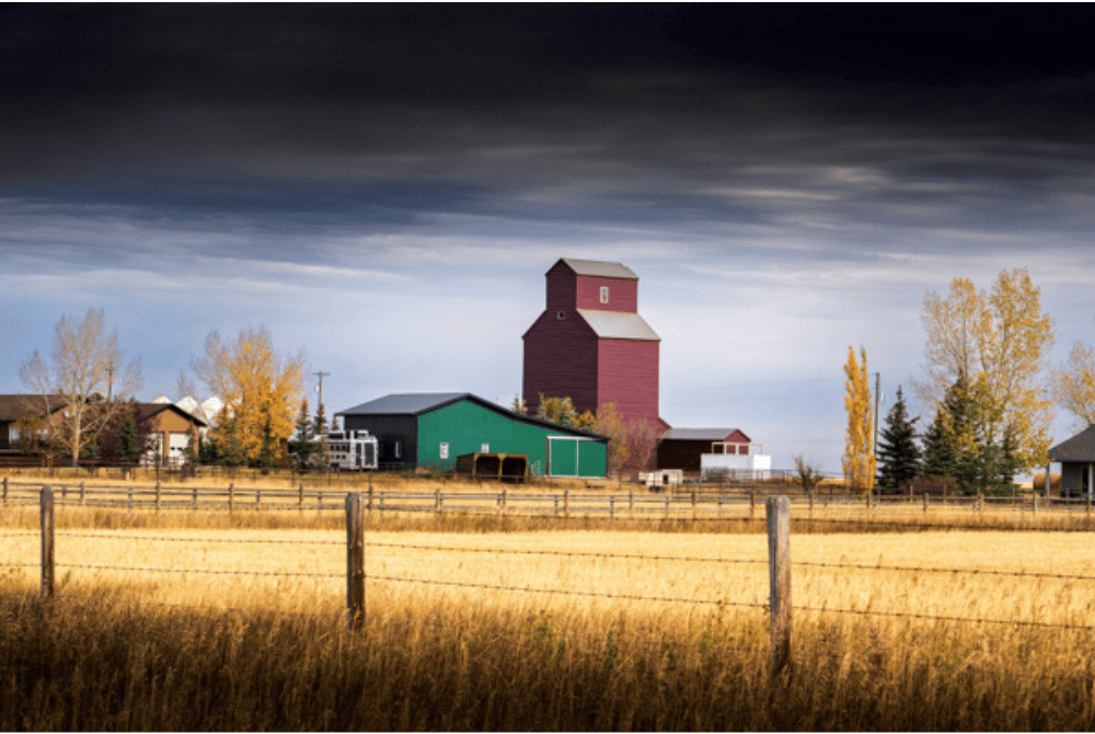 Rural landscape with a red grain elevator, farm buildings, and fenced grassland 