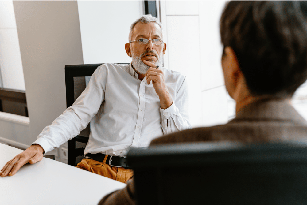 Two people seated across from each other in an office meeting, with one person listening thoughtfully