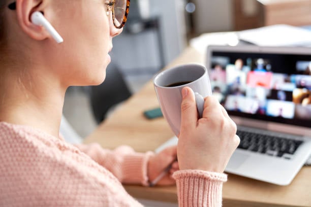 Young woman drinking coffee watching a webinar