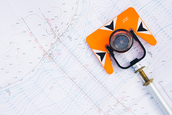 orange theodolite prism lies on a background geodetic maps